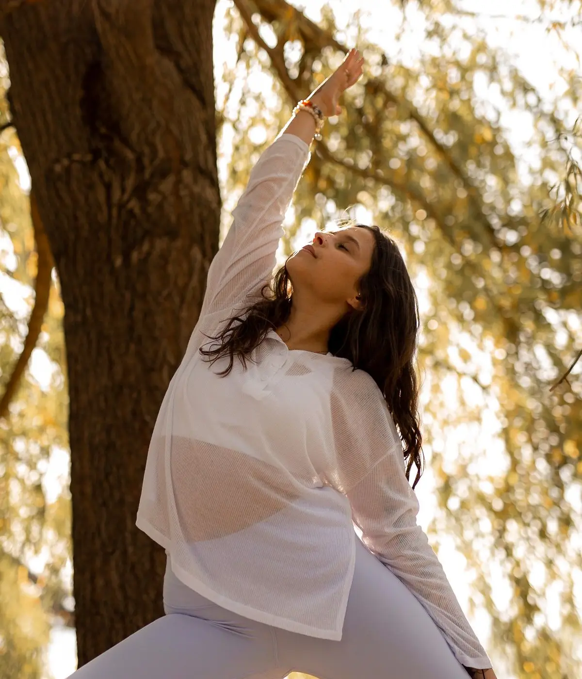 Christina en flexion latérale debout, un bras levé vers la lumière, sous un saule