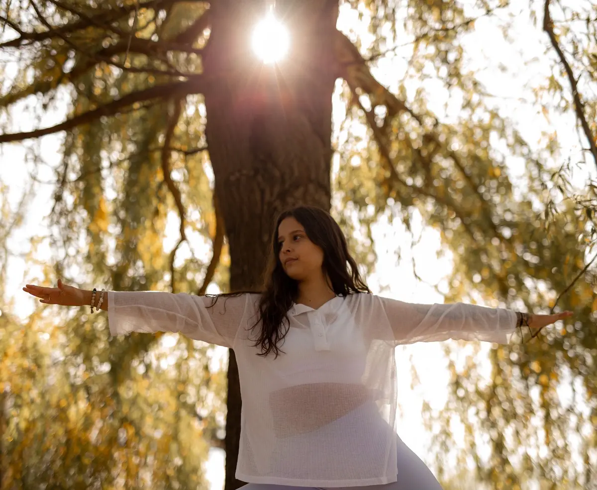 Christina debout bras étendus de chaque côté, le soleil derrière l’arbre